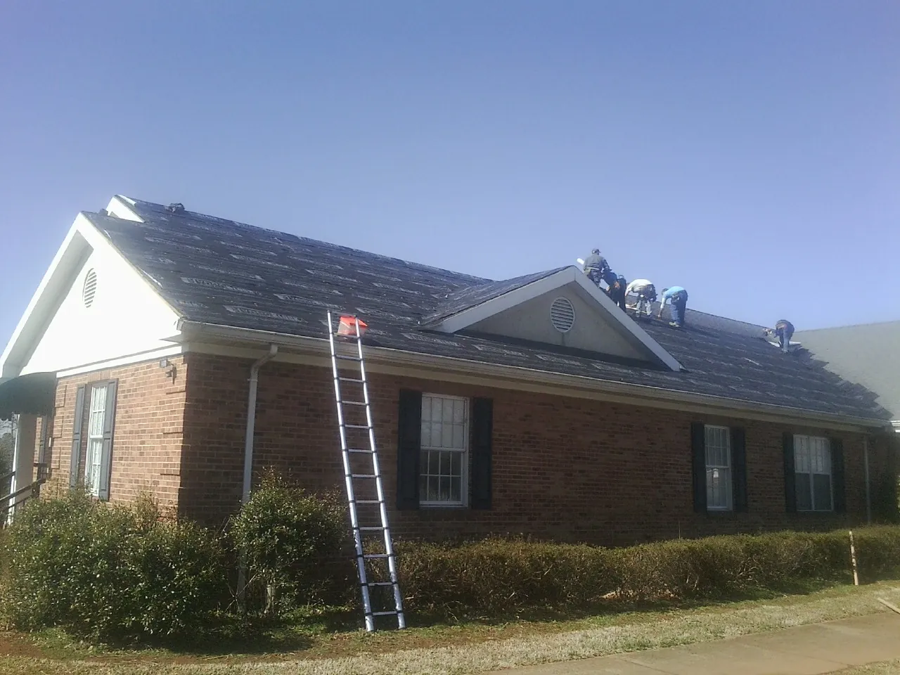 Crew tearing shingles off a brick ranch roof with a ladder set — Emergency Roof Repair work by our crew in Signal Mountain