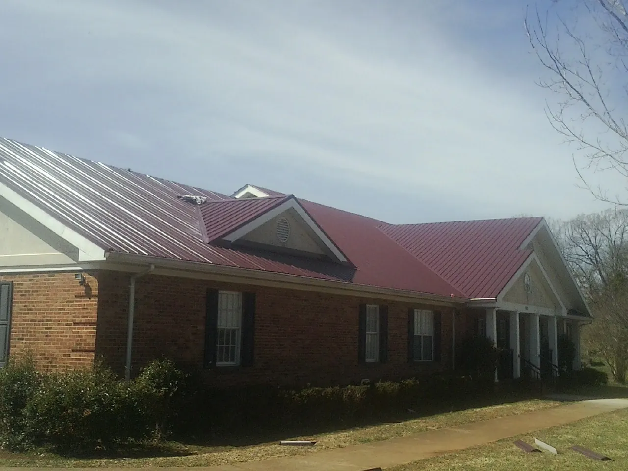 Red metal roof with gabled entries on a long brick building, from a Hail Damage Roof Repair job in Signal Mountain