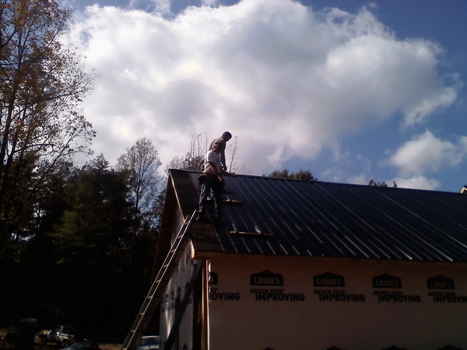 Roofer fastening dark metal panels high against a cloudy sky, from a Roof Inspection job in Signal Mountain
