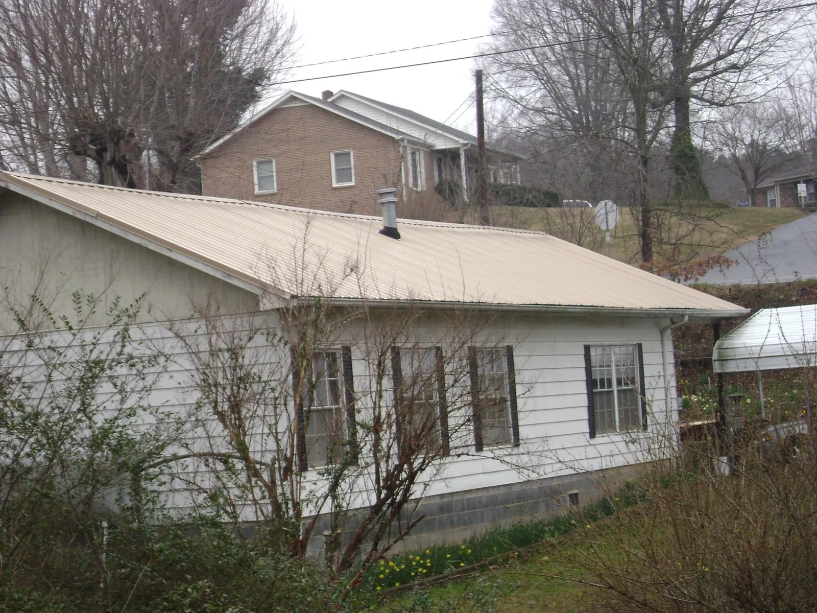 Tan metal roof on a white sided house set into a hillside — Commercial Roofing by Roofing Brothers in Signal Mountain